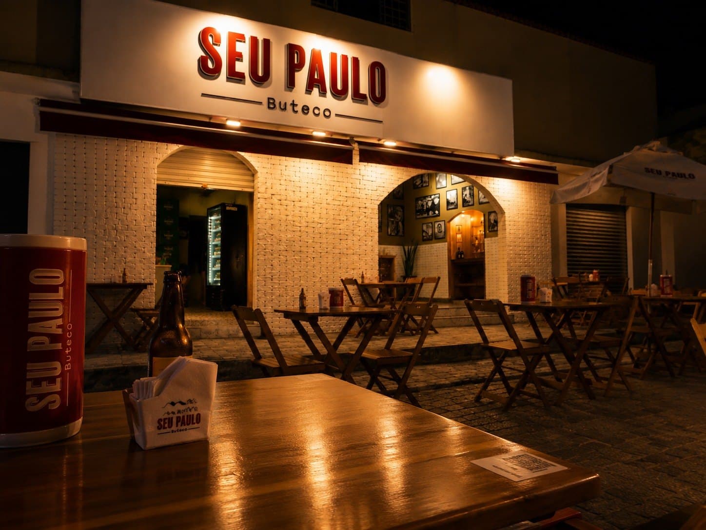 Mesa na calçada do buteco, com copo e porta-guardanapos da casa
